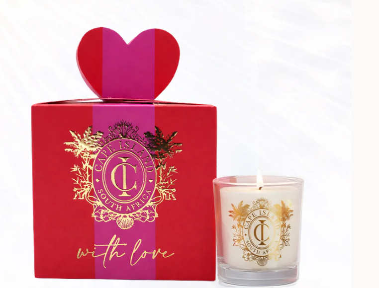 A Mini fragrant Cape island candle in a clear glass holder with a gold crest label, shown next to its red gift box with a heart-shaped lid and gold foil detailing. 